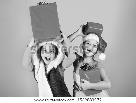 Kids in Santa Claus hats with gift boxes open presents. Childhood leisure and xmas sale concept. Children with joyful faces play on blue background. Girls celebrate Christmas