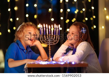 Kids celebrating Hanukkah. Jewish festival of lights. Children lighting candles on traditional menorah. Boy in kippah with dreidel and Sufganiyah doughnut. Israel holiday.