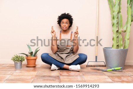 Gardener woman sitting on the floor with fingers crossing and wishing the best