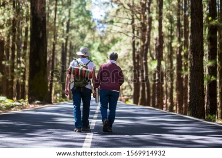 Travel lifestyle for old senior couple walking together in the middle of the road with high trees forest on both sides - lifestyle and togetherness forever life concept - aged people