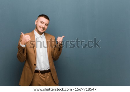 young handsome man smiling joyfully and looking happy, feeling carefree and positive with both thumbs up against flat background