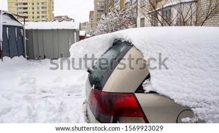 The car, covered with thick layer of snow. Negative consequence of heavy snowfalls. Side hundred cars with different patterns.