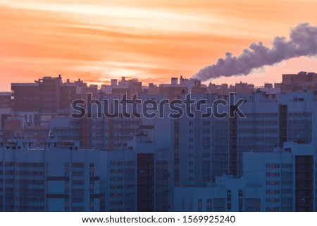 The buildings of the new district or block and steam of the electric power station on the background of setting or rising sun in the morning or in the evening in the cold winter weather