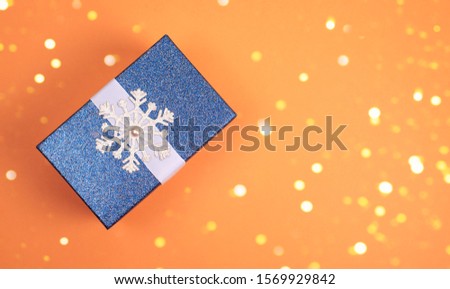 Blue shiny Christmas gift with snowflake on orange background. A festive composition. Christmas photo.