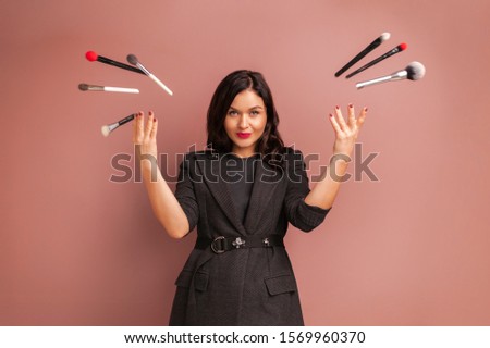 Studio photo of makeup artist woman smiling and throws up brushes and tools over a beige background. Professional makeup training concept. Idea for advertising