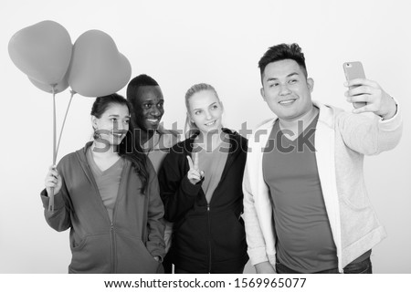 Happy diverse group of multi ethnic friends taking selfie together while holding heart shaped balloons ready for Valentine's day