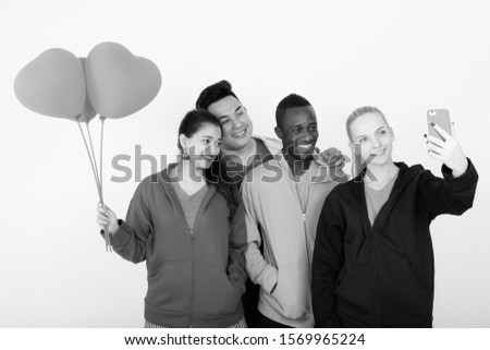 Happy diverse group of multi ethnic friends taking selfie together while holding heart shaped balloons ready for Valentine's day