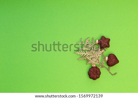 Christmas composition. Christmas decorations red shiny Christmas toys star, heart and flower with a branch of a golden Christmas tree on a bright green horizontal background. Minimalist concept for yo