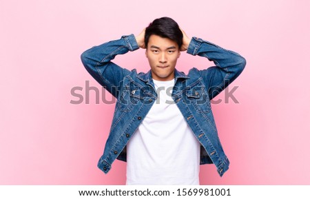 young chinese man feeling frustrated and annoyed, sick and tired of failure, fed-up with dull, boring tasks against flat color wall