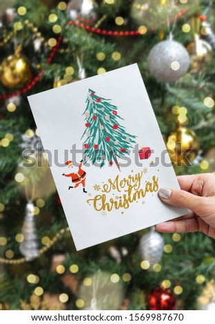 Hand holding christmas holiday greeting card on christmas tree background.