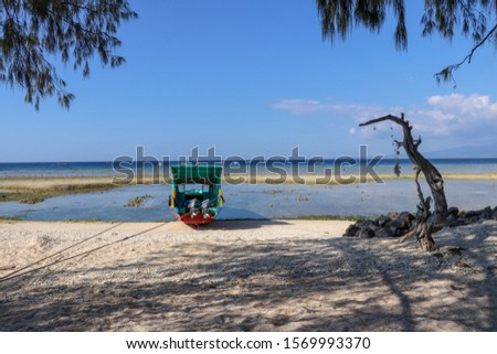 Relaxing atmosphere on the ocean shore. White fine sand and tethered fishing boat offshore at low tide time. Wooden boat with green roof. Old withered tree stump twisted into abstract shape.