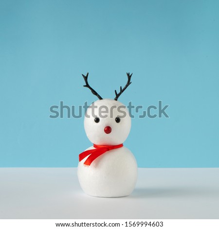 Snowman on bright blue background with reindeer nose and antlers. Winter holiday concept. Christmas minimal idea.
