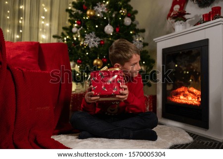 boy near the christmas tree and fireplace opens gifts