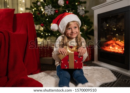 girl near the christmas tree and fireplace opens gifts