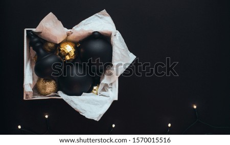 Close up box with vintage Christmas black and golden decorations and festive lights on black background.