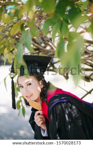 Soft, selective focus of Asian woman graduation smiling and holding in her hands yellow leaves hiding her chin over under tree