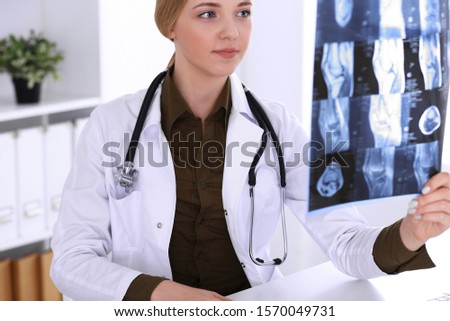 Doctor woman examining x-ray picture near window in hospital. Surgeon or orthopedist at work. Medicine and healthcare concept. Khaki colored blouse of a therapist looks good
