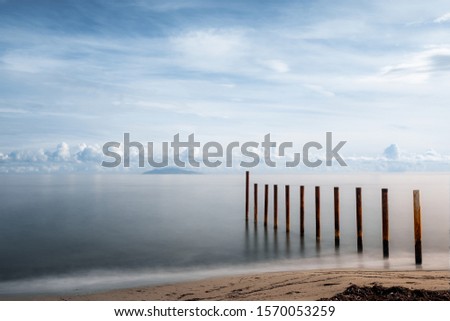 Long exposure image of breakwater on a beach in Corsica silhouetted by the early morning sun against a calm Mediterranean sea with the island of Elba in the distance