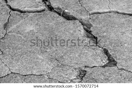 A high resolution old concrete cement with cracks and natural destruction from time and weather conditions. Non-color, monochrome black and white photo.