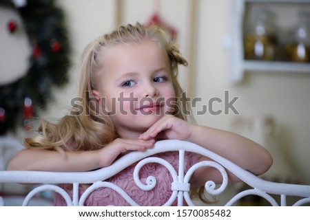 cute little blonde girl in pink dress with beautiful haircut leaning on the railing of the bed