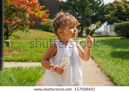 Cute baby girl is blowing a dandelion