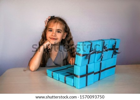 Cute little girl near a huge pile of blue gift boxes formed like a laptop over white studio background, she dreaming about travel, season holiday wish concept