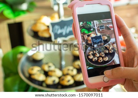 The cafe owner uses a smartphone to take pictures of newly finished cupcakes to promote on online media and websites. Selling products online
