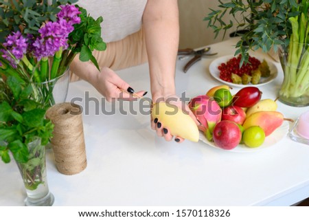 photo from a series of pictures about the process of forming a fruit and flower bouquet. tutorial, do it yourself. photo 13, women's hands inserts long wooden skewers into yellow mango