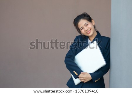 A working woman is carrying a laptop and she smiles. Cute. Looks happy.