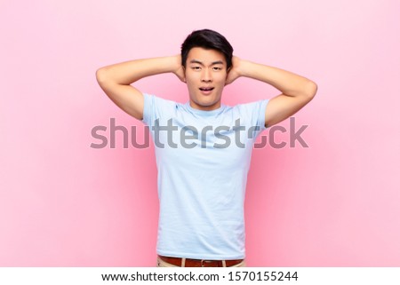 young chinese man looking happy, carefree, friendly and relaxed enjoying life and success, with a positive attitude against flat color wall
