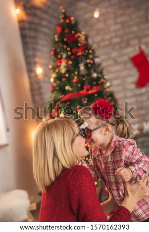Beautiful mother and daughter wearing Christmas party glasses, hugging and having fun at home while celebrating Christmas