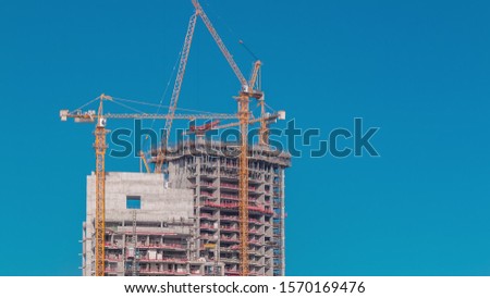 Aerial view of a skyscrapers under construction with huge cranes timelapse in Dubai marina. Blue sky on a background. United Arab Emirates