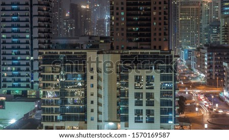 Dubai Marina with illuminated skyscrapers and promenade aerial night timelapse. Modern towers and boats from above with traffic on a road. United Arab Emirates