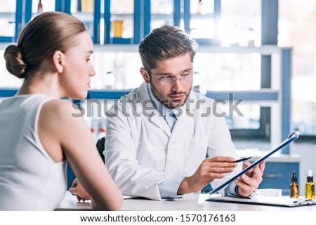 selective focus of allergist holding clipboard near patient in clinic  Royalty-Free Stock Photo #1570176163