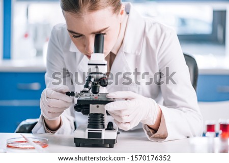 attractive immunologist looking through microscope in laboratory  Royalty-Free Stock Photo #1570176352