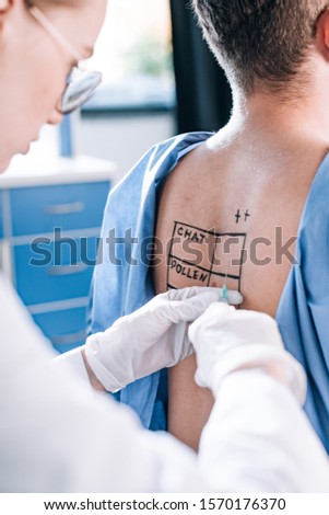 cropped view of allergist in latex gloves holding syringe near man with marked back 
