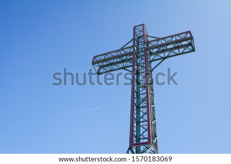 Cross metal structure in blue sky in public park. Illuminated Steel cross