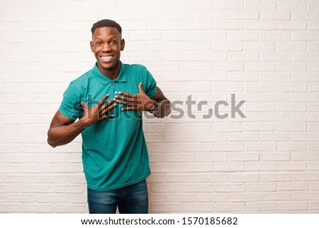 young african american black man looking happy, surprised, proud and excited, pointing to self against brick wall