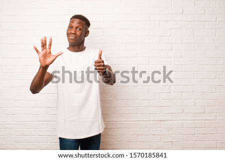 young african american black man smiling and looking friendly, showing number six or sixth with hand forward, counting down against brick wall