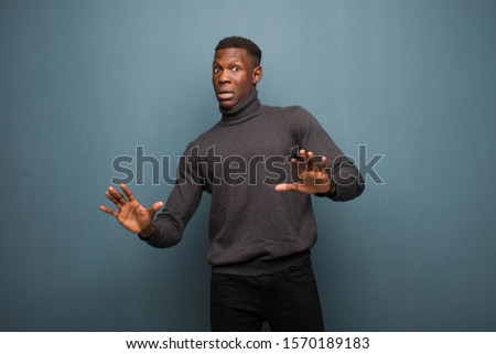 young african american black man feeling stupefied and scared, fearing something frightening, with hands open up front saying stay away against grunge wall Royalty-Free Stock Photo #1570189183