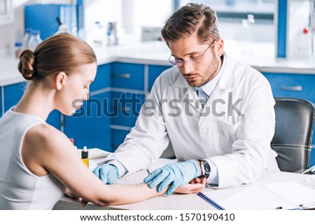 selective focus of handsome allergist holding ruler near marked hand of woman  Royalty-Free Stock Photo #1570190410