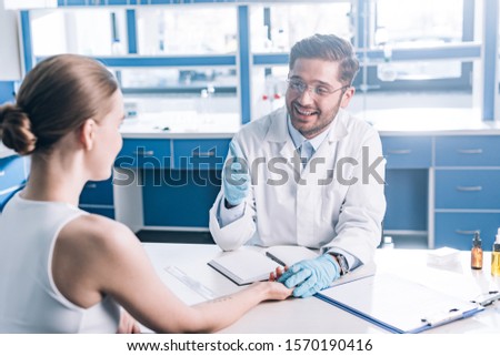 selective focus of happy doctor showing thumb up and holding hand of woman in clinic Royalty-Free Stock Photo #1570190416