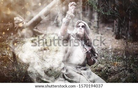 Fairy magician. A sorcerer with a glass sphere, a magical spell and a ritual. Elder with a staff and a cross in the forest. Black and white magic. A spell in old book.
