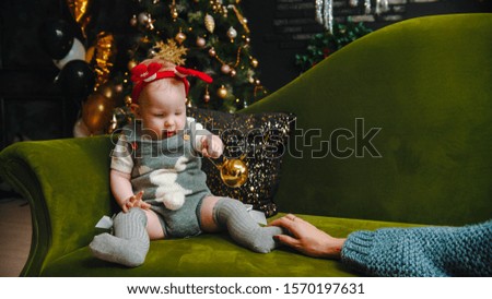 NEW YEAR - baby is sitting on sofa and playing with christmas ball