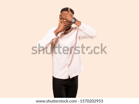 young african american black man covering face with both hands saying no to the camera! refusing pictures or forbidding photos against beige wall