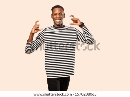 young african american black man framing or outlining own smile with both hands, looking positive and happy, wellness concept against beige wall