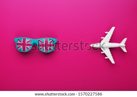 Turquoise sunglasses with United Kingdom flag in lenses on crazy pink background with white airplane. 