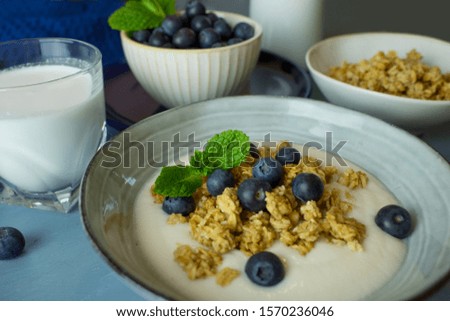 Food photography of a ceramic bowl with yogurt, granola cereal and blueberries on a blue background.