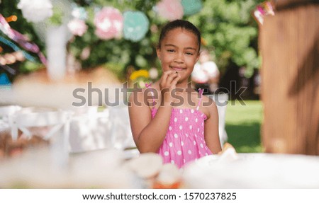 Small girl standing outdoors in garden in summer, birthday celebration concept.