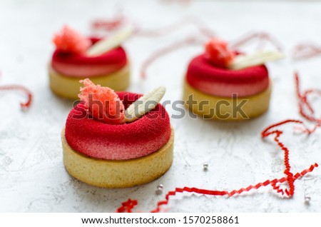 Set of contemporary raspberry mini mousse tarts covered with red velvet spray decorated with chocolate feathers on light background